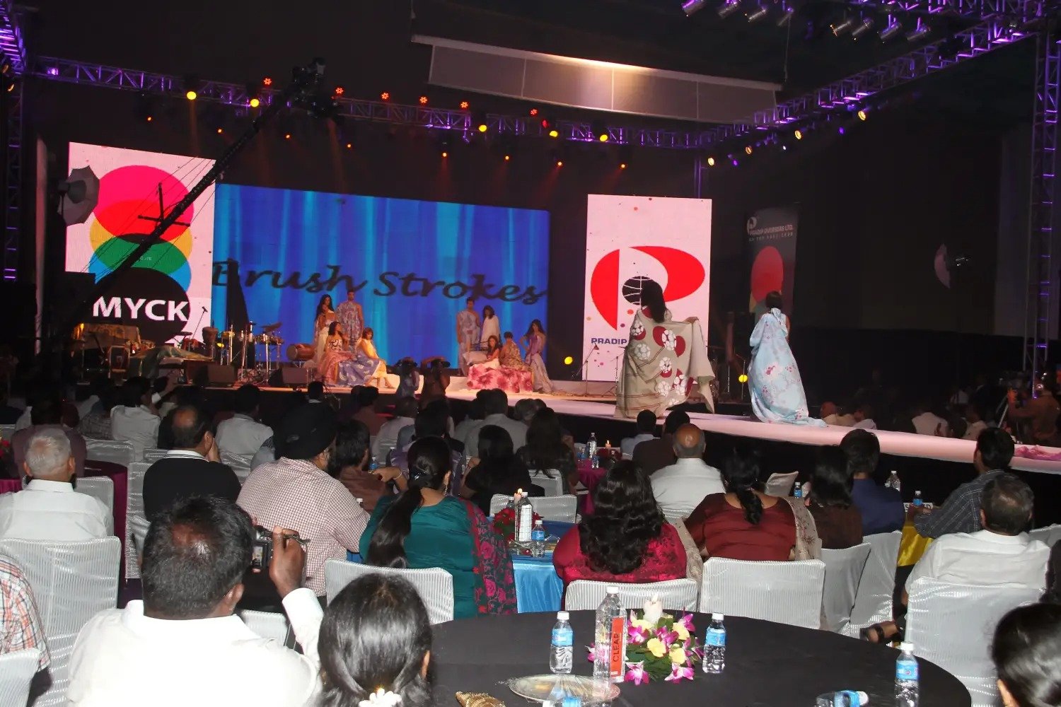 Man and woman speaking on stage at night with blue lighting